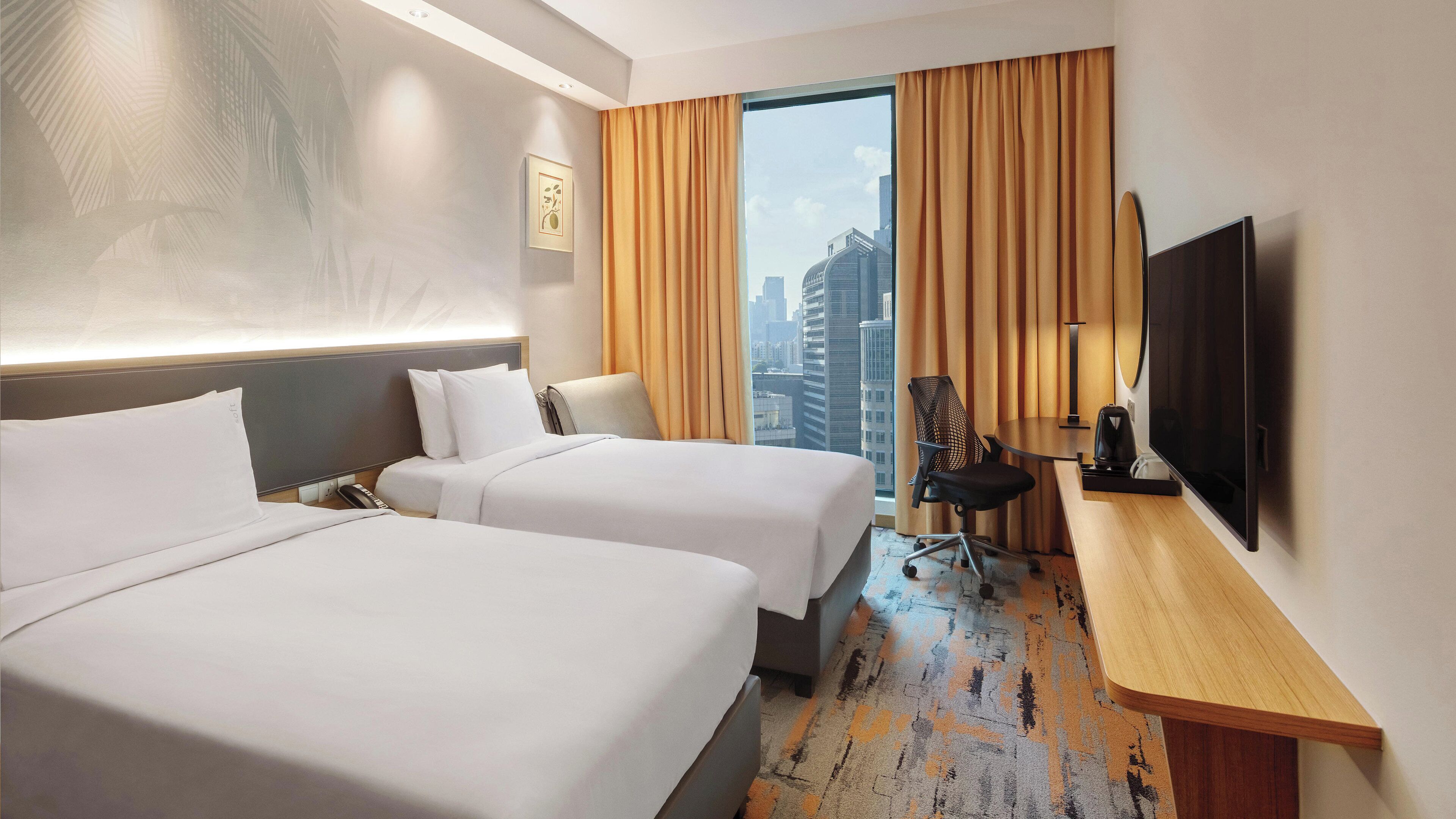 A hotel room with two beds, a desk, a chair, a television, and a city view.