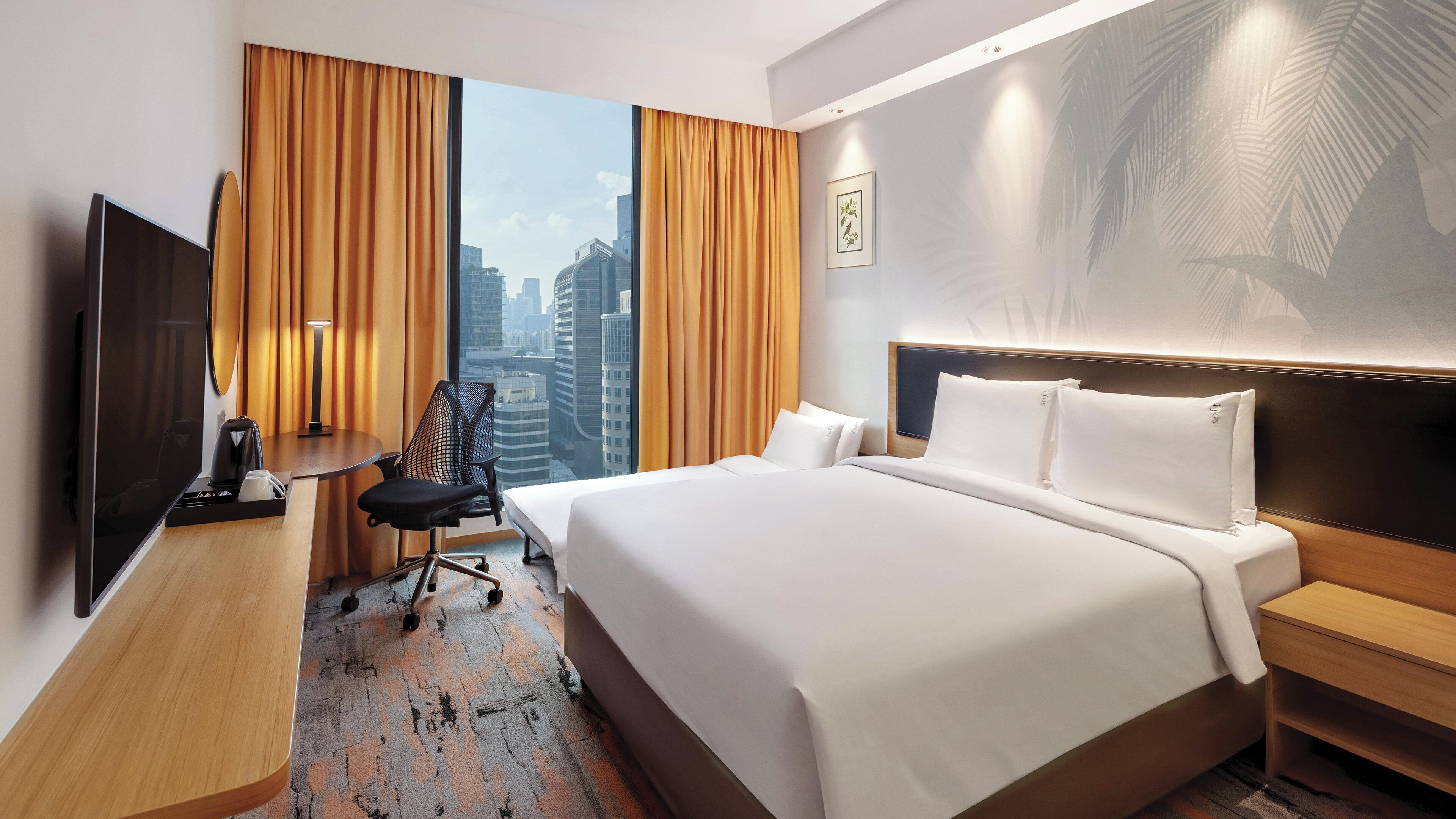Ein Hotelzimmer mit einem großen Bett, einem Schreibtisch mit Stuhl, einem Fernseher und Blick auf die Stadt.