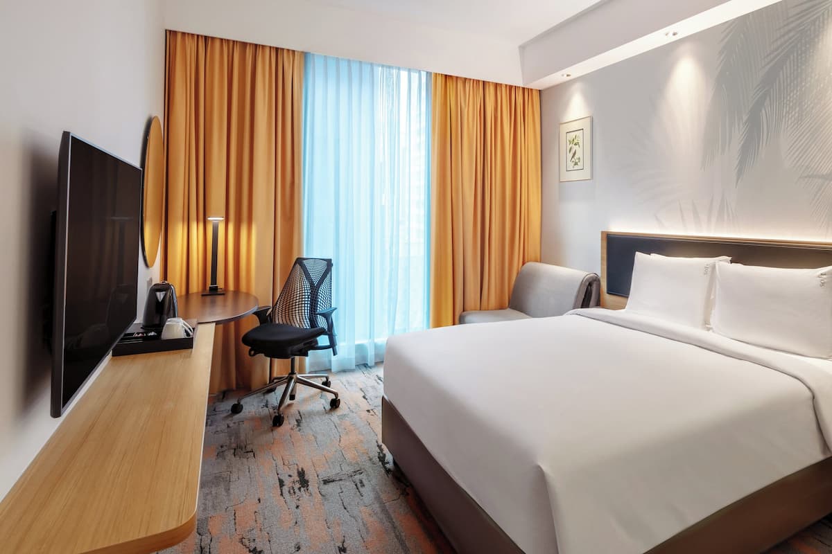 A hotel room with a large bed, a desk with a chair, a TV, and a window with curtains.