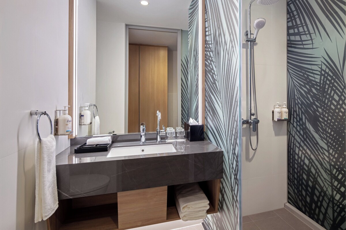 Un baño moderno con un espejo grande, un lavabo de mármol oscuro, una ducha con puerta de cristal y un perchero para toallas.
