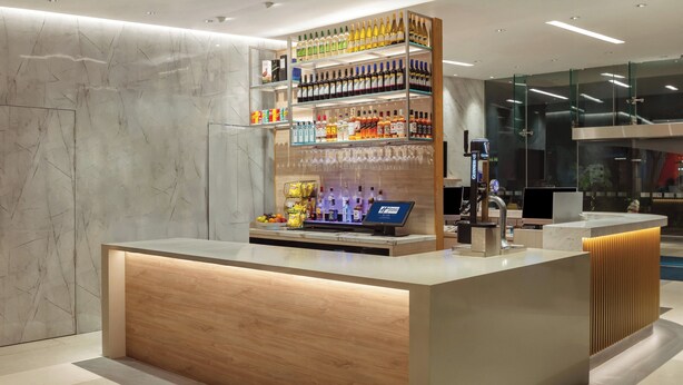 Un comptoir d’accueil moderne avec un revêtement en bois, une vitrine en verre contenant diverses bouteilles et un kiosque numérique.