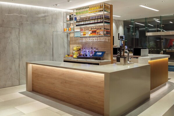 Een moderne receptiebalie met een houten afwerking, een glazen vitrine met diverse flessen en een digitale kiosk.