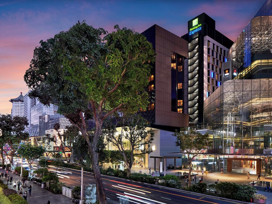 Et moderne hotel med et tydeligt Holiday Inn Express skilt, omgivet af bygninger og en travl gade i skumringen.