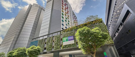 Un edificio moderno con un llamativo letrero de 'Holiday Inn Express', que presenta un jardín vertical y una vista despejada del cielo.