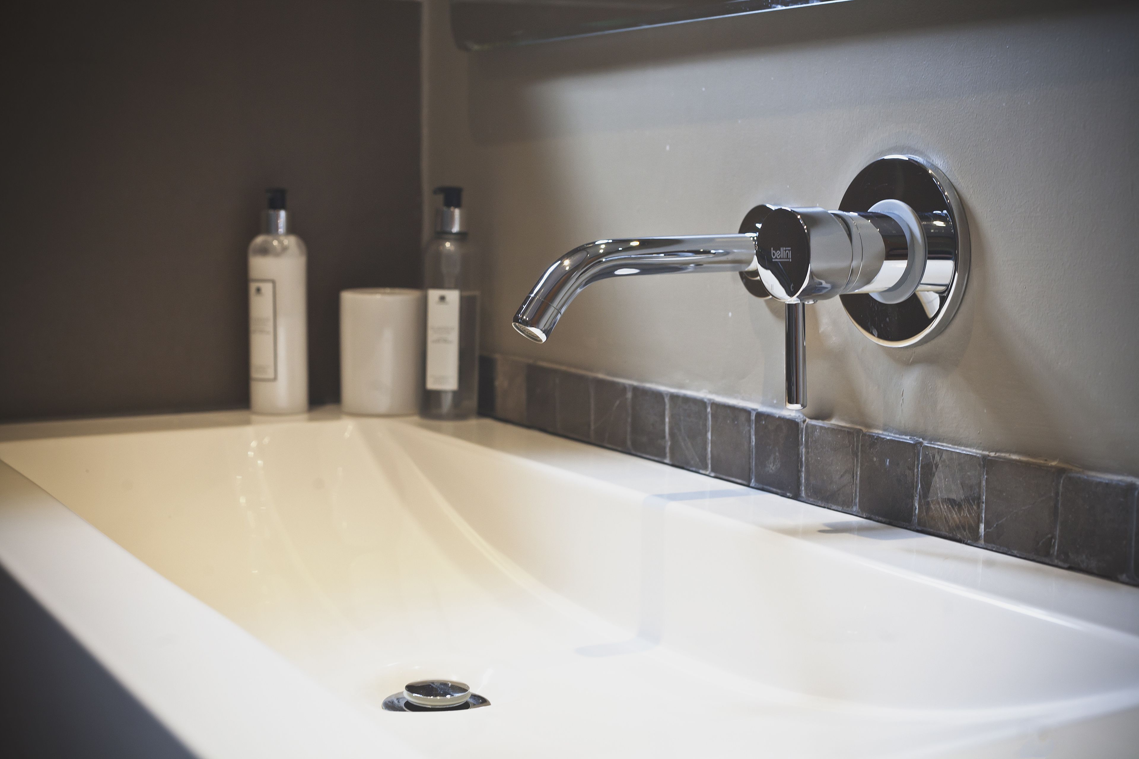 A modern bathroom with a chrome faucet, a white sink, and a tiled backsplash.