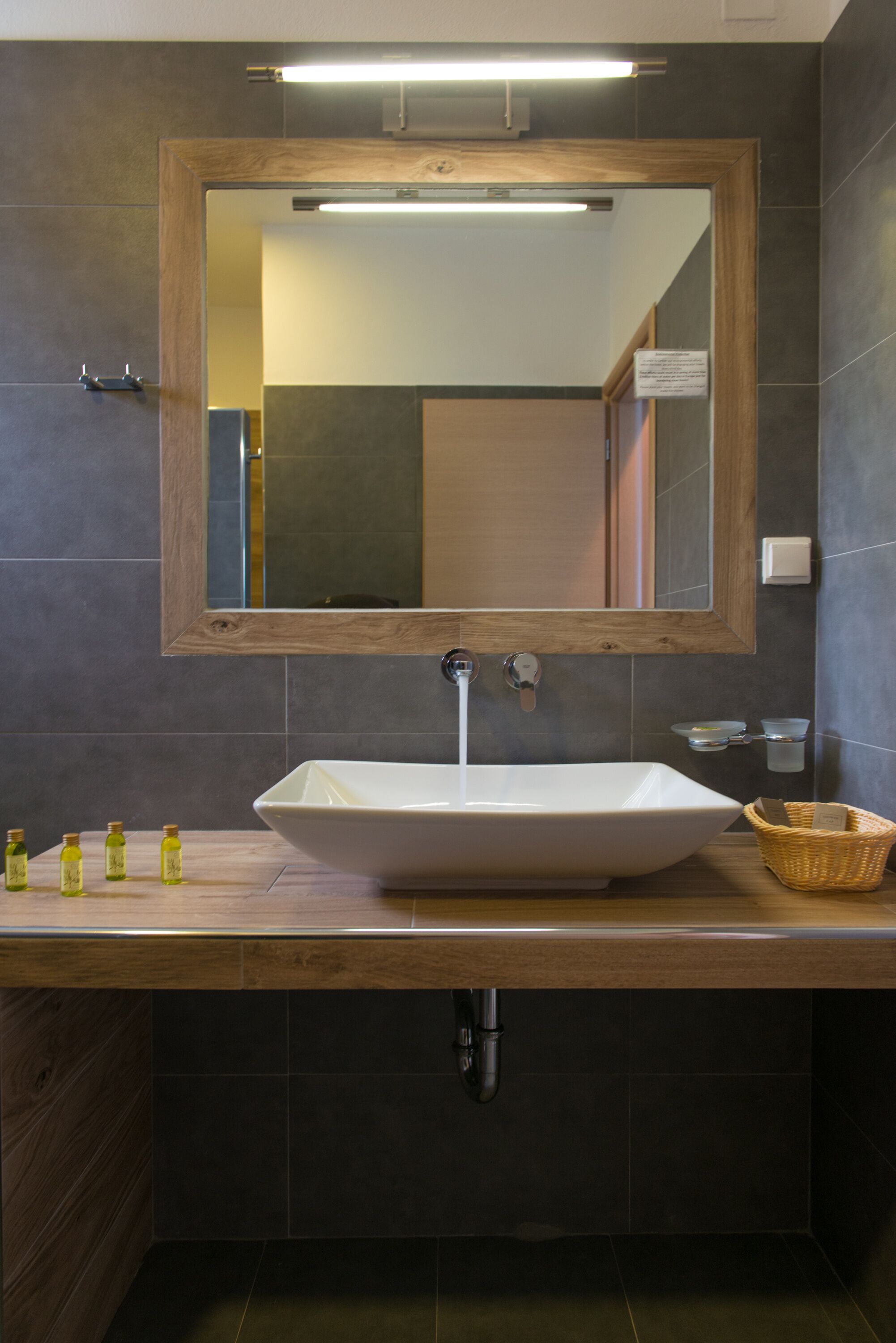 Une salle de bain avec un meuble-lavabo en bois, un grand miroir et un lavabo sur colonne.