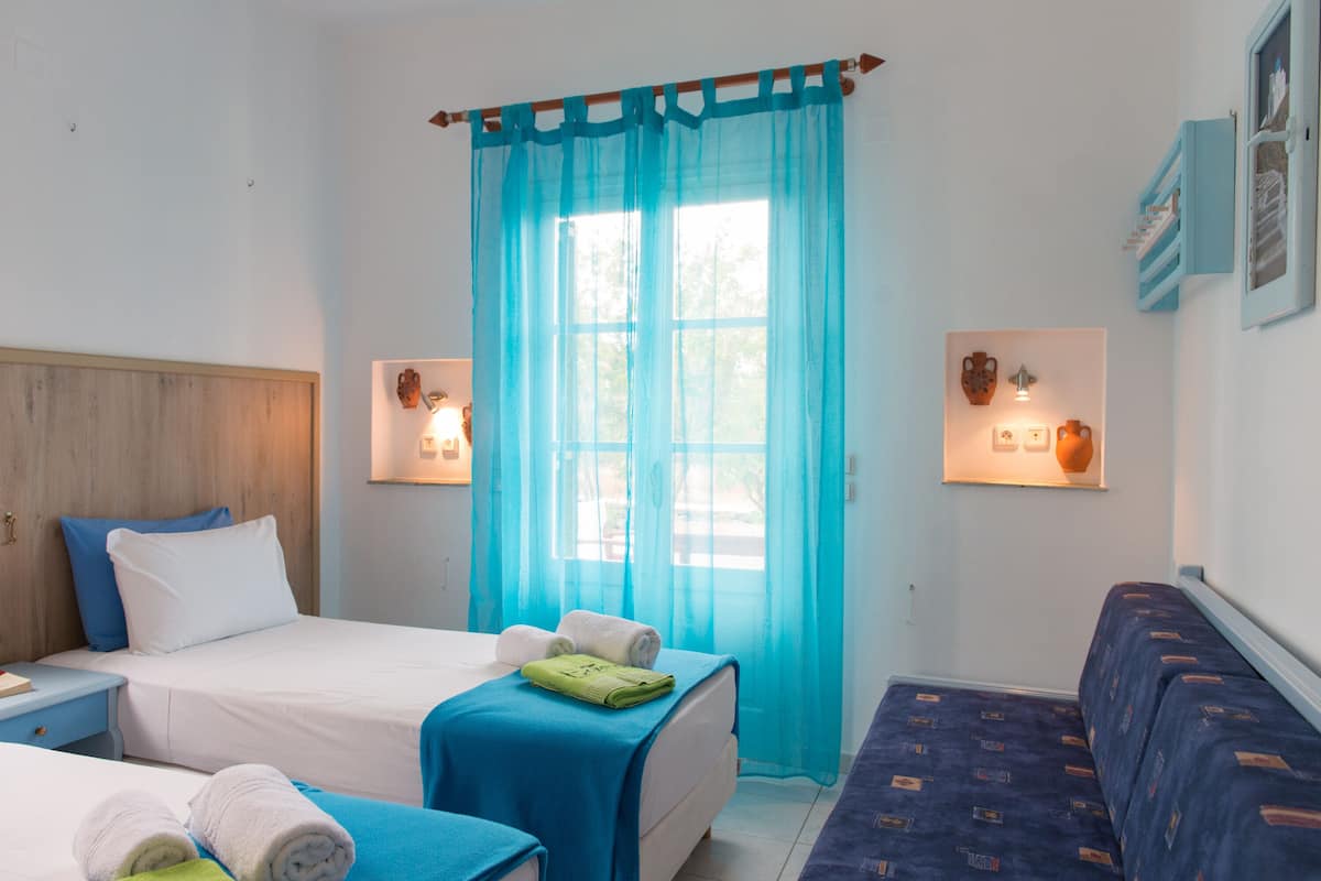 A hotel room with two beds, a sofa, a window with blue curtains, and wall-mounted lights.
