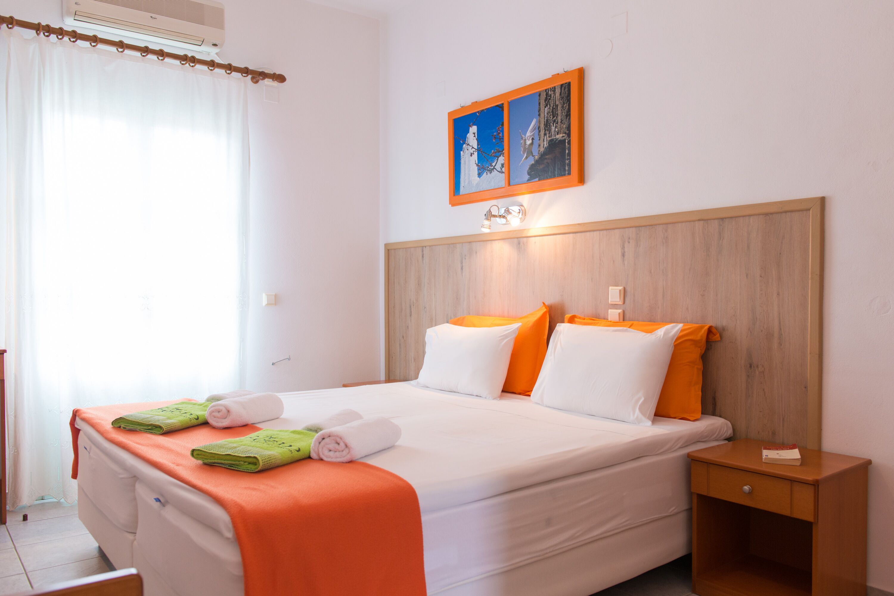 Habitació d'hotel amb un llit, una taula de nit, un quadre a la paret i una finestra amb cortines.