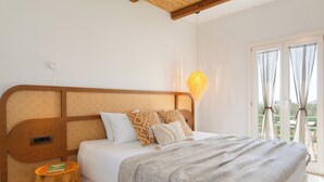 Een net opgemaakt bed met gestreepte kussens, een nachtkastje met een boek en een hanglamp.