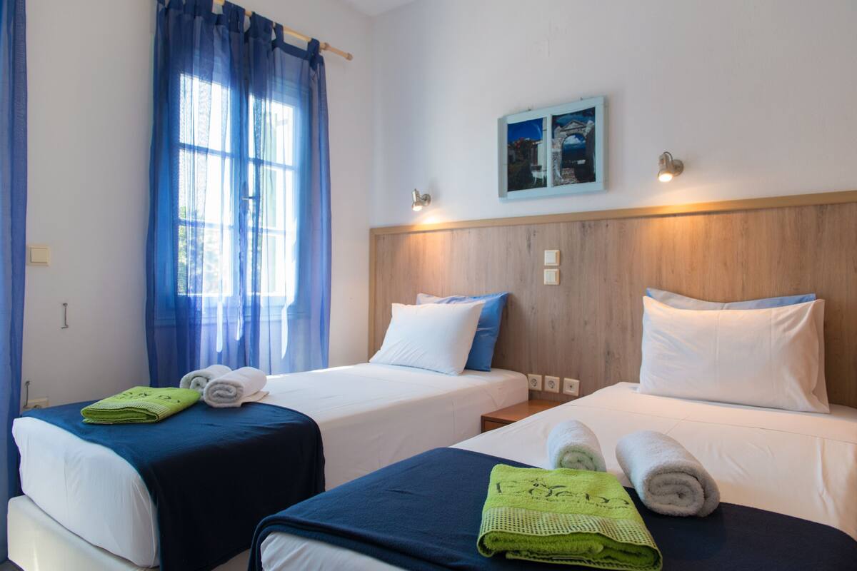 A hotel room with two beds, each with a blue and white bedspread, and a wooden headboard. There are towels on the beds and a painting on the wall.