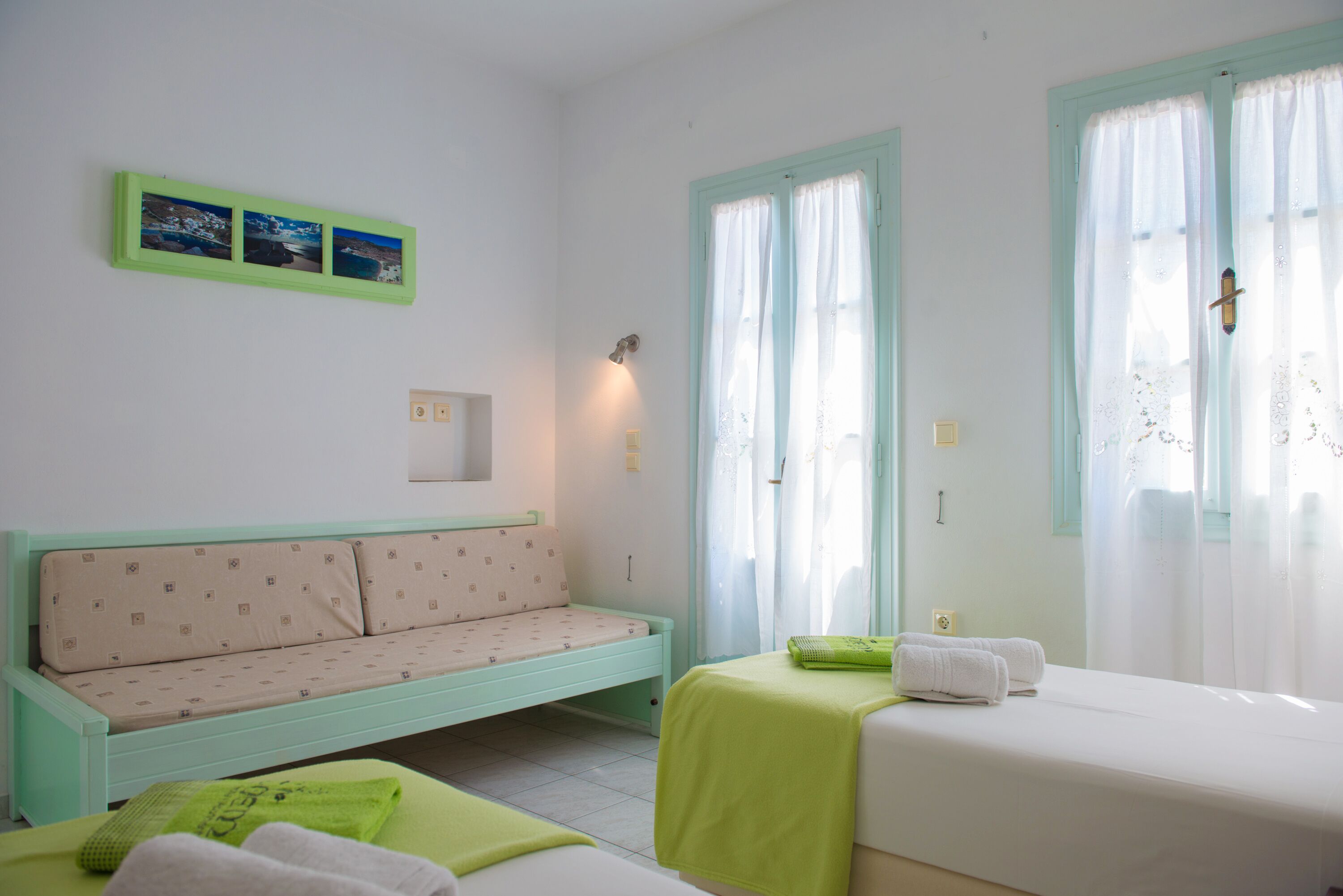 A room with a bed, a sofa, a small table with towels, and a wall-mounted light.