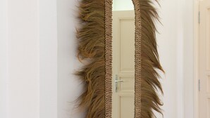 Een kamer met een grote, gestructureerde spiegel en een houten kruk.