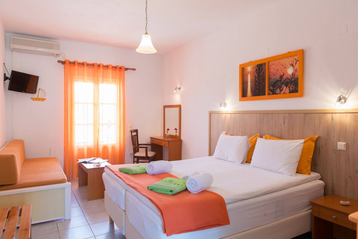 A hotel room with a bed, a desk, a chair, a TV, and a window with curtains.