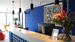 En receptionsdisk med en blå tapetvæg, en dekorativ vægpanel og en vase med blomster.