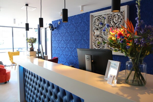 Una recepción con un muro azul estampado, un panel decorativo y un jarrón con flores.