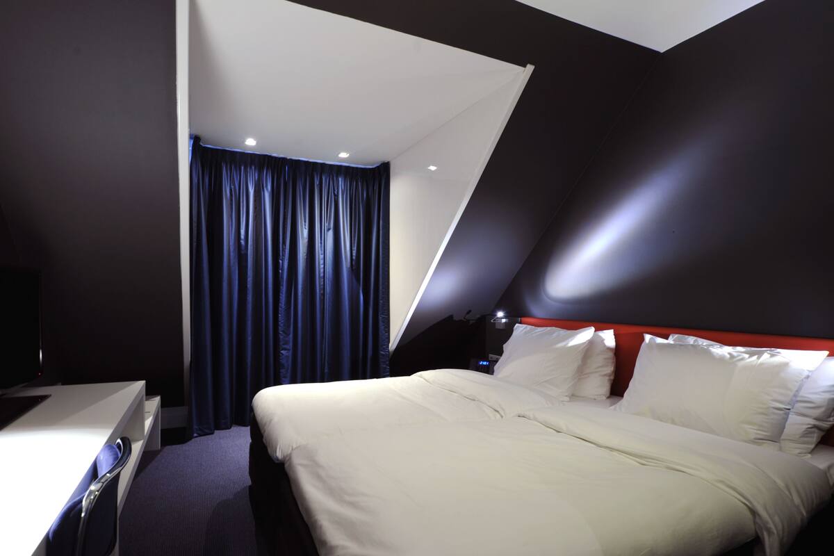 Een moderne hotelkamer met een bed, bureau en een groot raam met gordijnen.