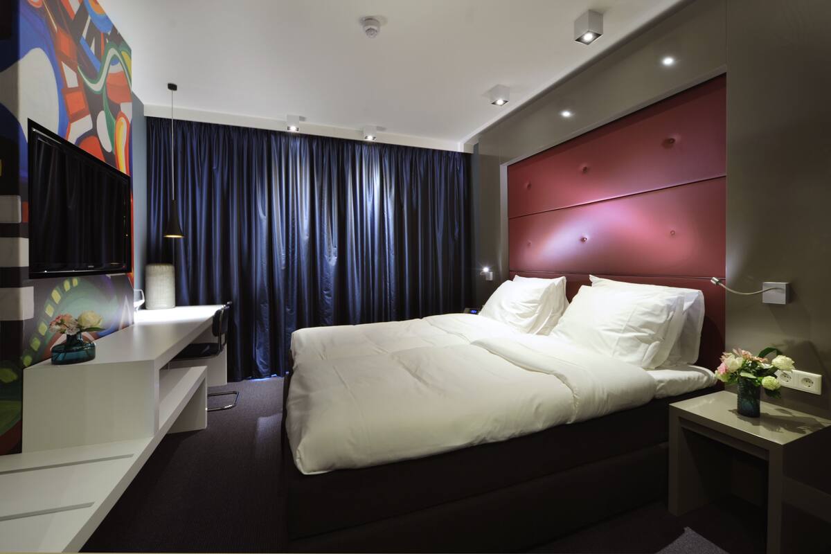 Een moderne hotelkamer met een groot bed, een flatscreen-televisie, een bureau en een rode hoofdeinde.