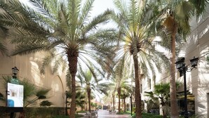 A paved walkway lined with palm trees and a brick floor, leading to a building entrance. - Madareem Hotel (Riyadh)
