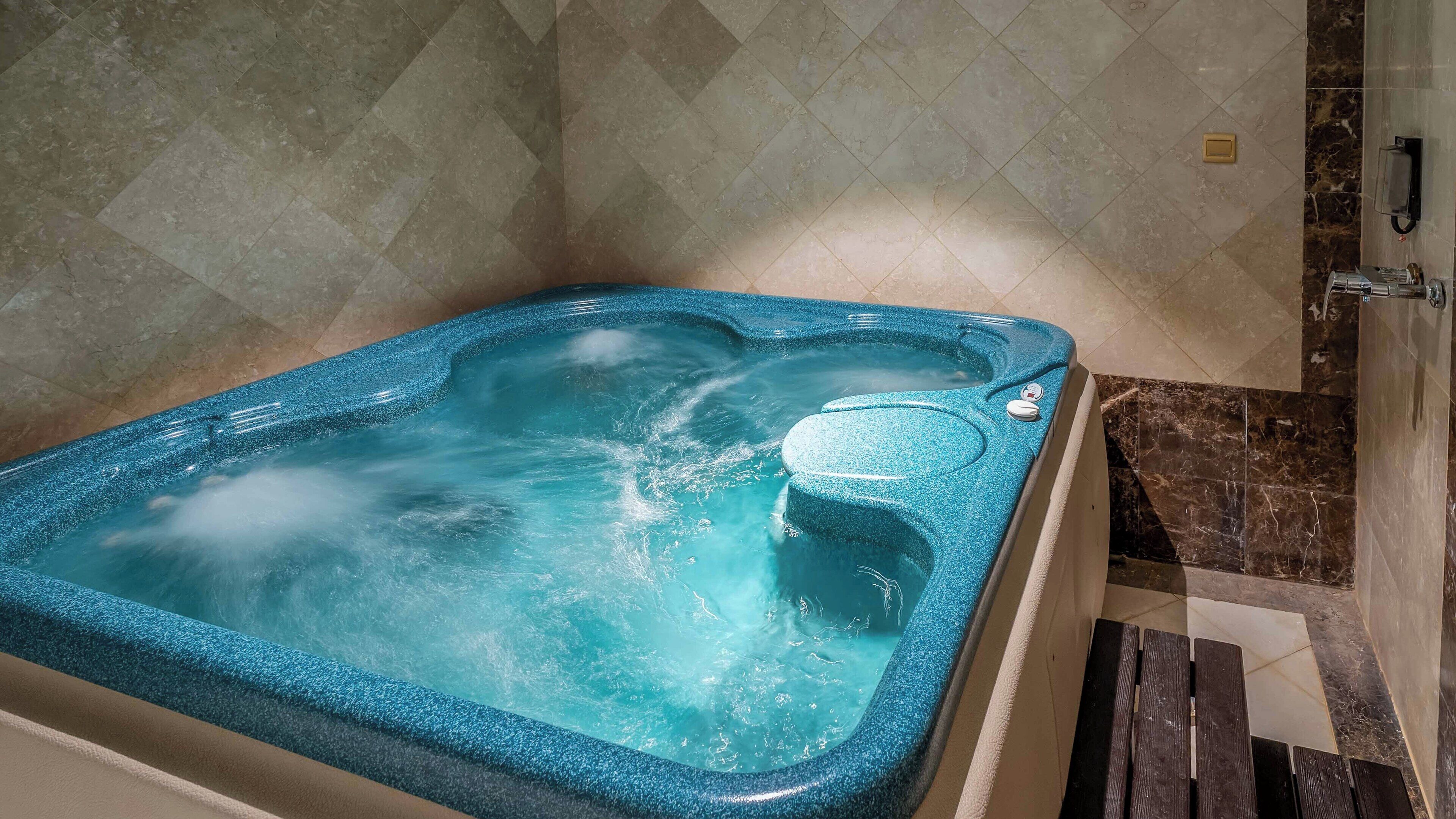 Un espace de bien-être comprenant un jacuzzi, des murs en marbre et un sol en marbre.