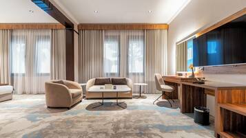 Una habitación de hotel moderna con sofá, sillones, una mesita, escritorio y televisor.