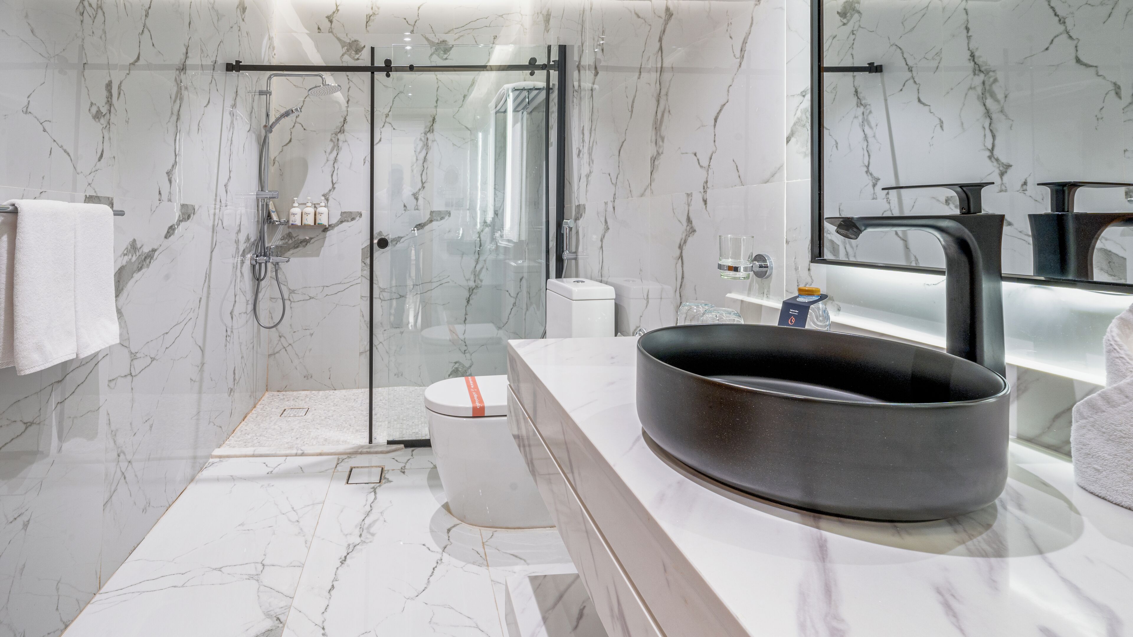 A modern bathroom with a glass-enclosed shower, a large black sink, and marble walls.