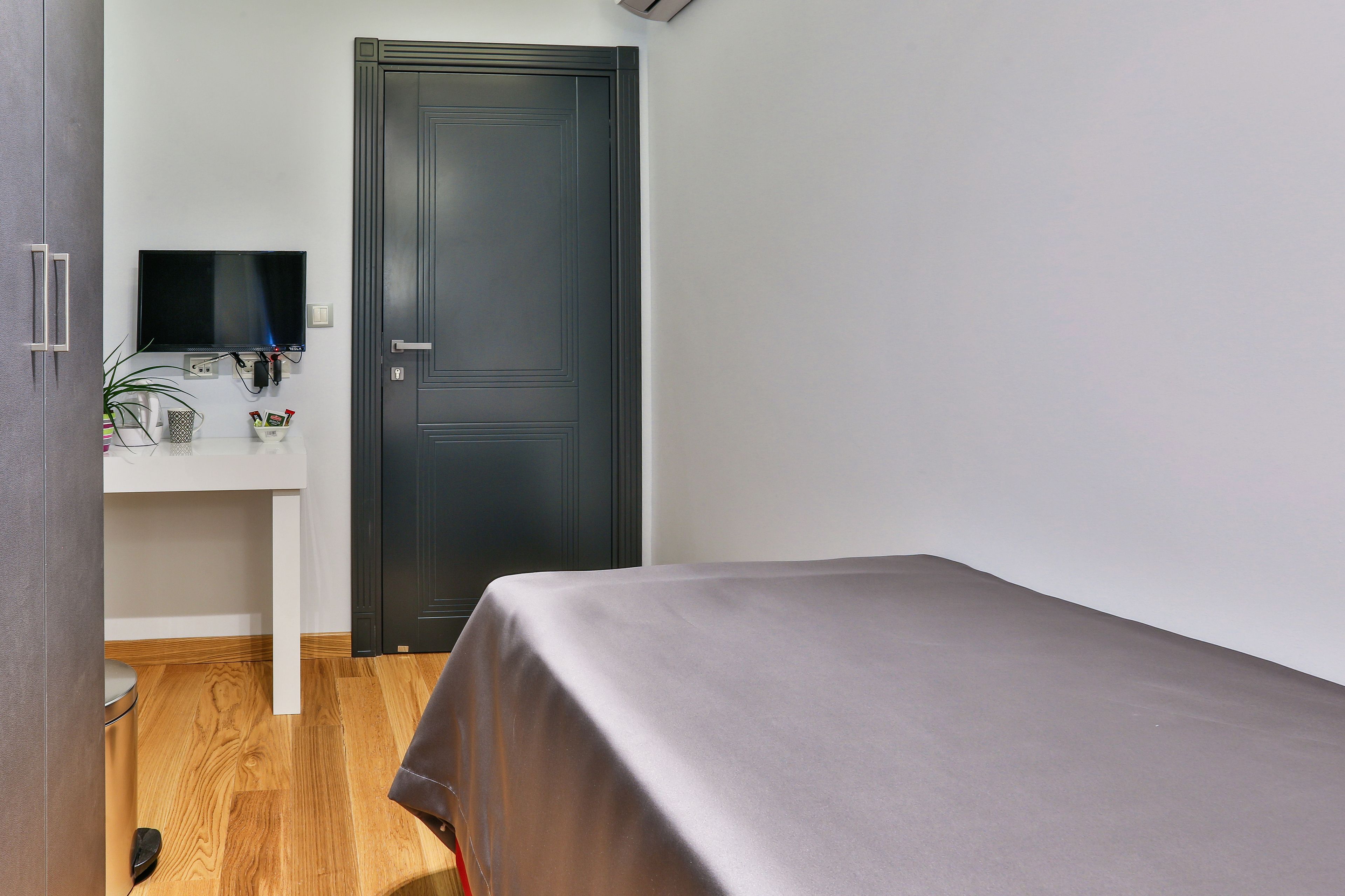 A room with a bed, a desk with a TV, and a door.