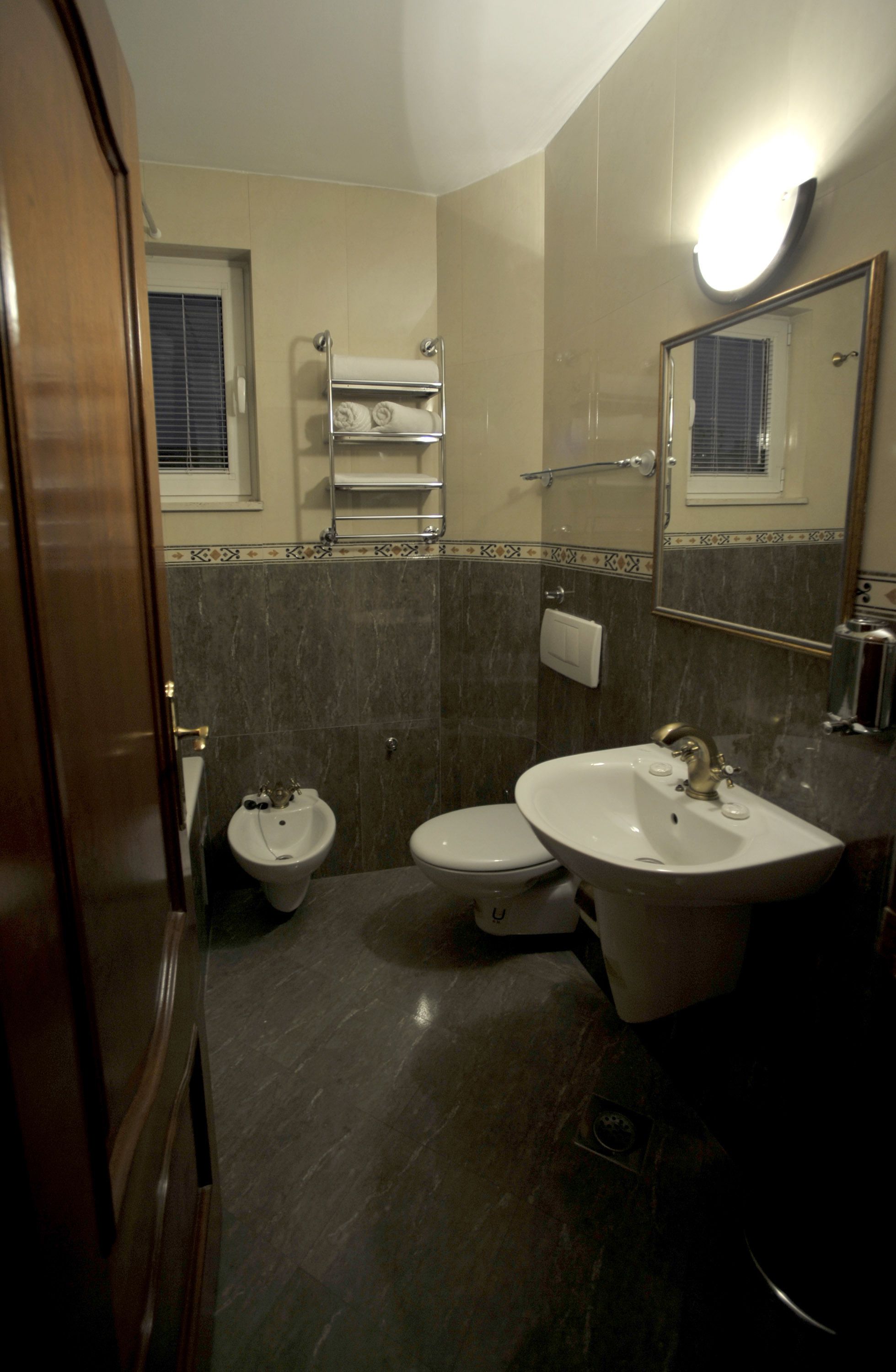 A bathroom with a bidet, toilet, and sink. There is a towel rack above the toilet and a mirror above the sink.