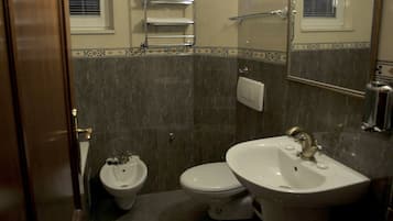 A bathroom with a bidet, toilet, and sink. There is a towel rack above the toilet and a mirror above the sink.