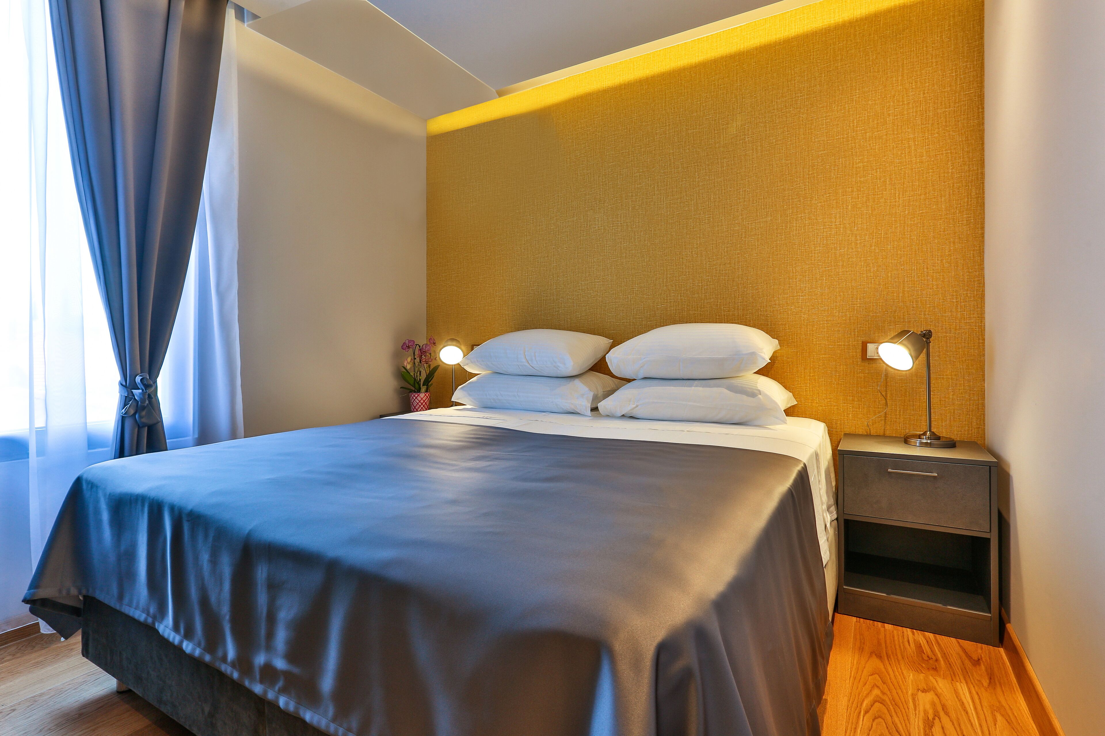 Ein ordentlich bezogenes Bett mit einer dunkelblauen Tagesdecke, ein Nachttisch mit Lampe und eine Wand mit einer strukturierten Oberfläche.