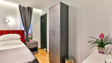 A modern bedroom with a bed, a wardrobe, a bedside table with a lamp, and a potted plant.
