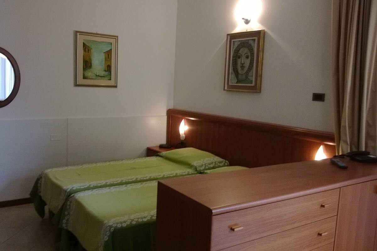Ein Zimmer mit zwei Einzelbetten, einem Holzschrank, einem runden Spiegel und zwei gerahmten Bildern an den Wänden.
