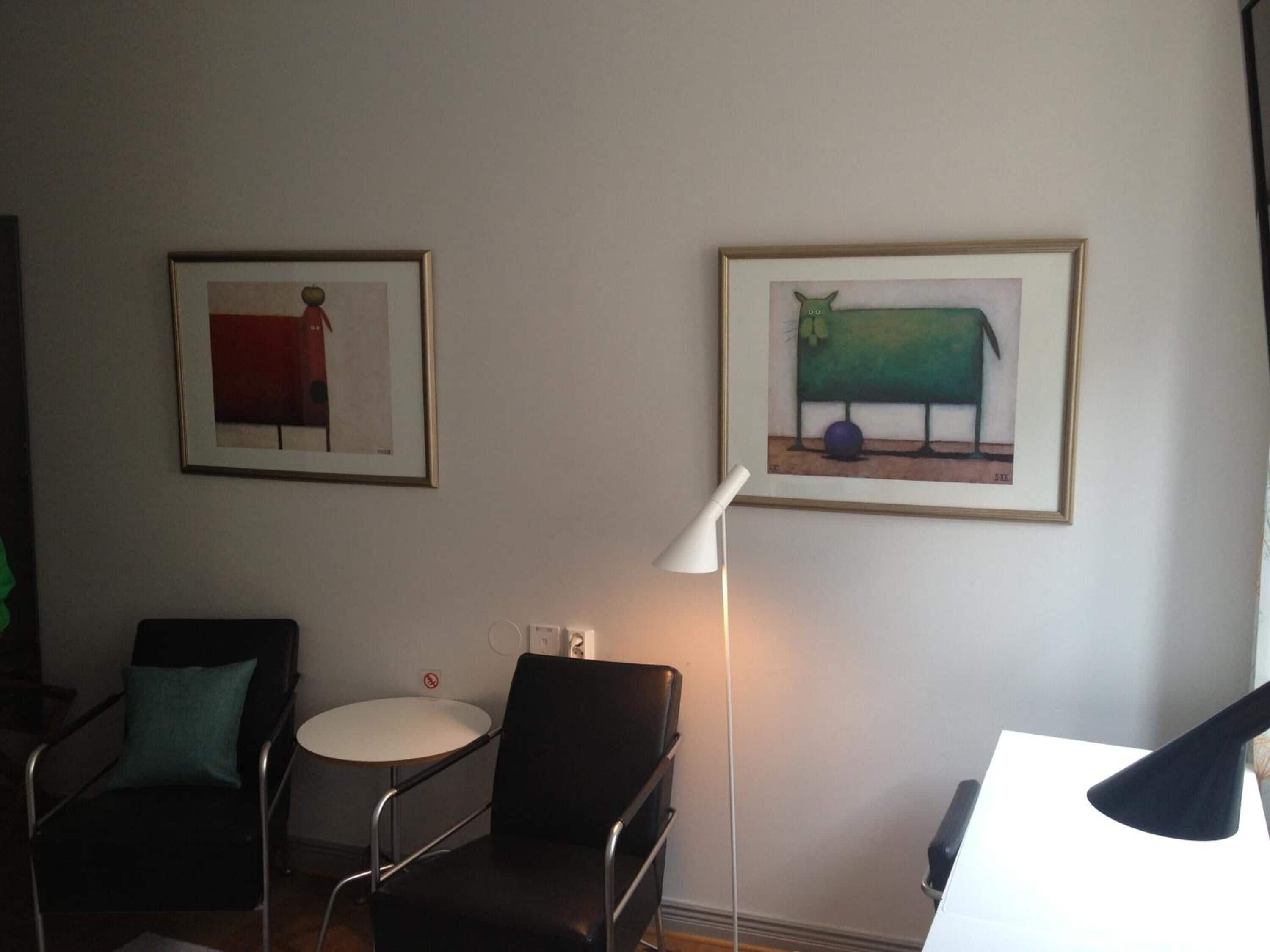 Ein Zimmer mit zwei schwarzen Stühlen, einem kleinen runden Tisch und zwei gerahmten Kunstwerken an der Wand.