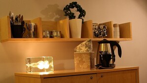 A wooden cabinet with a light fixture on top, a plant, and various kitchen items on shelves above. - Hotell Oskar (Lund)