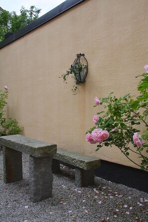 A stone bench and a wall-mounted lantern in a garden area. - Hotell Oskar (Lund)