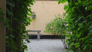 A gravel pathway leading to a bench and a building with a yellow wall. - Hotell Oskar (Lund)