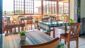 A restaurant with wooden tables and chairs, large windows, and potted plants. - Pousada dos Coqueiros Búzios (Búzios)