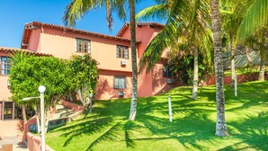 A building with a red facade, surrounded by well-maintained grass and palm trees. - Pousada dos Coqueiros Búzios (Búzios)