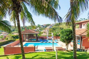A pool area with lounge chairs and a glass-enclosed structure, surrounded by palm trees and a hillside view. - Pousada dos Coqueiros Búzios (Búzios)