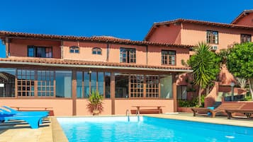 A pool area with lounge chairs and a building with large windows and a tiled roof.