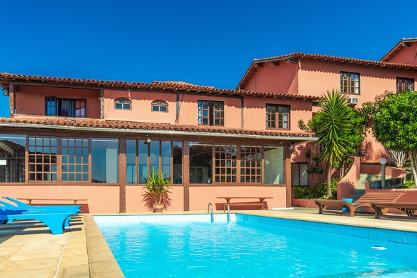 A pool area with lounge chairs and a building with large windows and a tiled roof. - Pousada dos Coqueiros Búzios (Búzios)
