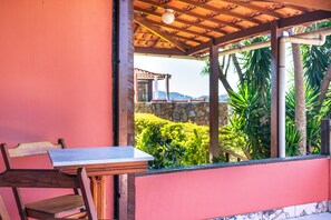 A covered outdoor seating area with a table and chairs, a stone wall, and lush greenery in the background. - Pousada dos Coqueiros Búzios (Búzios)