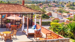 A rooftop terrace with a four-poster bed, wooden furniture, and a view of a hillside town. - Pousada dos Coqueiros Búzios (Búzios)