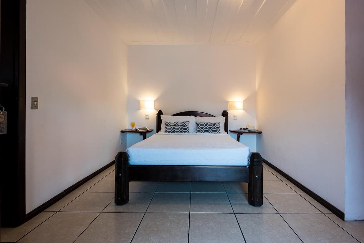 A bedroom with a bed, two bedside tables, and two wall-mounted lamps.
