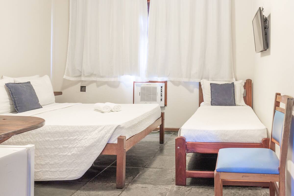 A hotel room with two beds, a small table, a chair, and a wall-mounted TV.