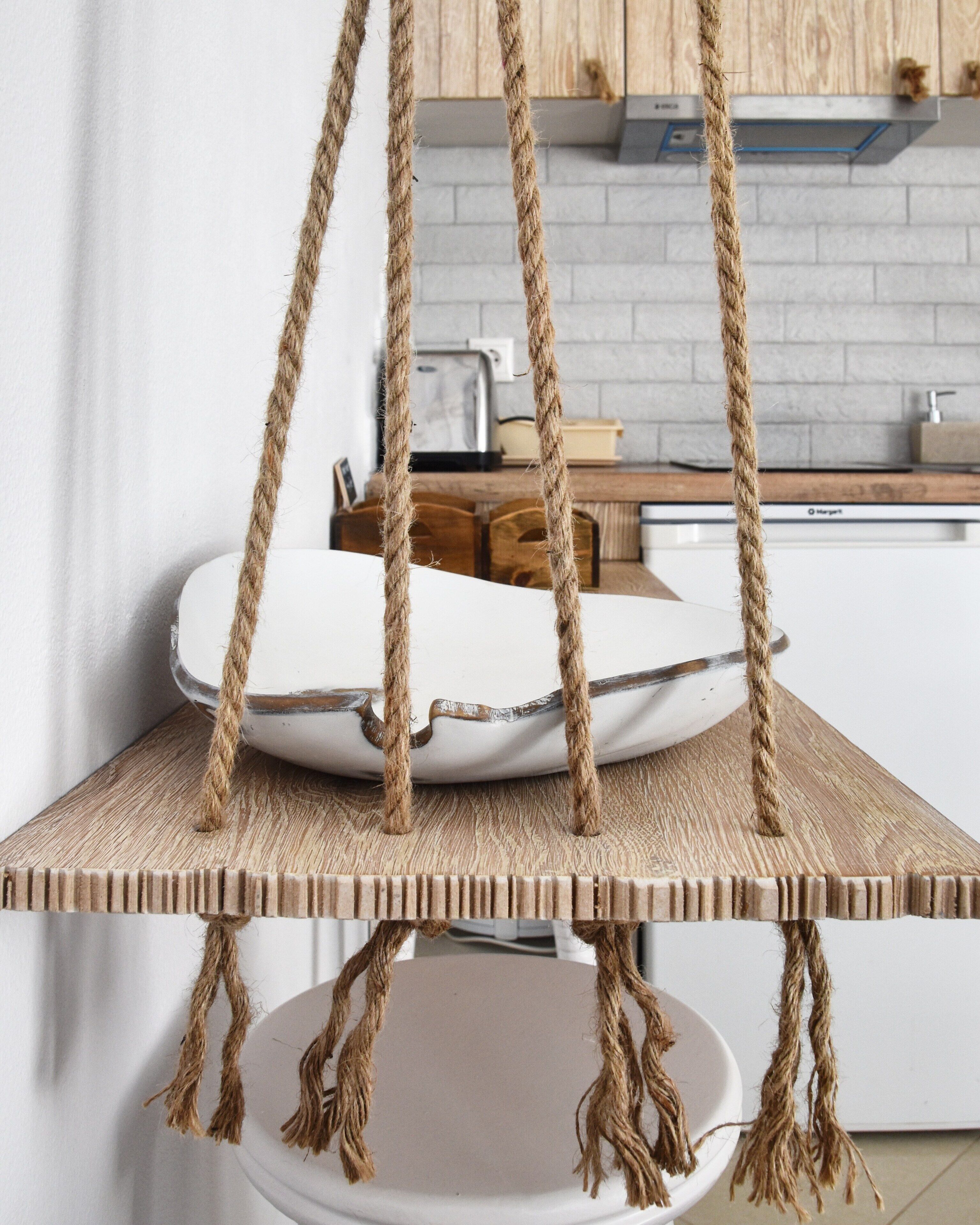 Una cocina con un estante de madera colgante sostenido por cuerdas, un plato blanco y un bloque de cuchillos sobre la encimera.