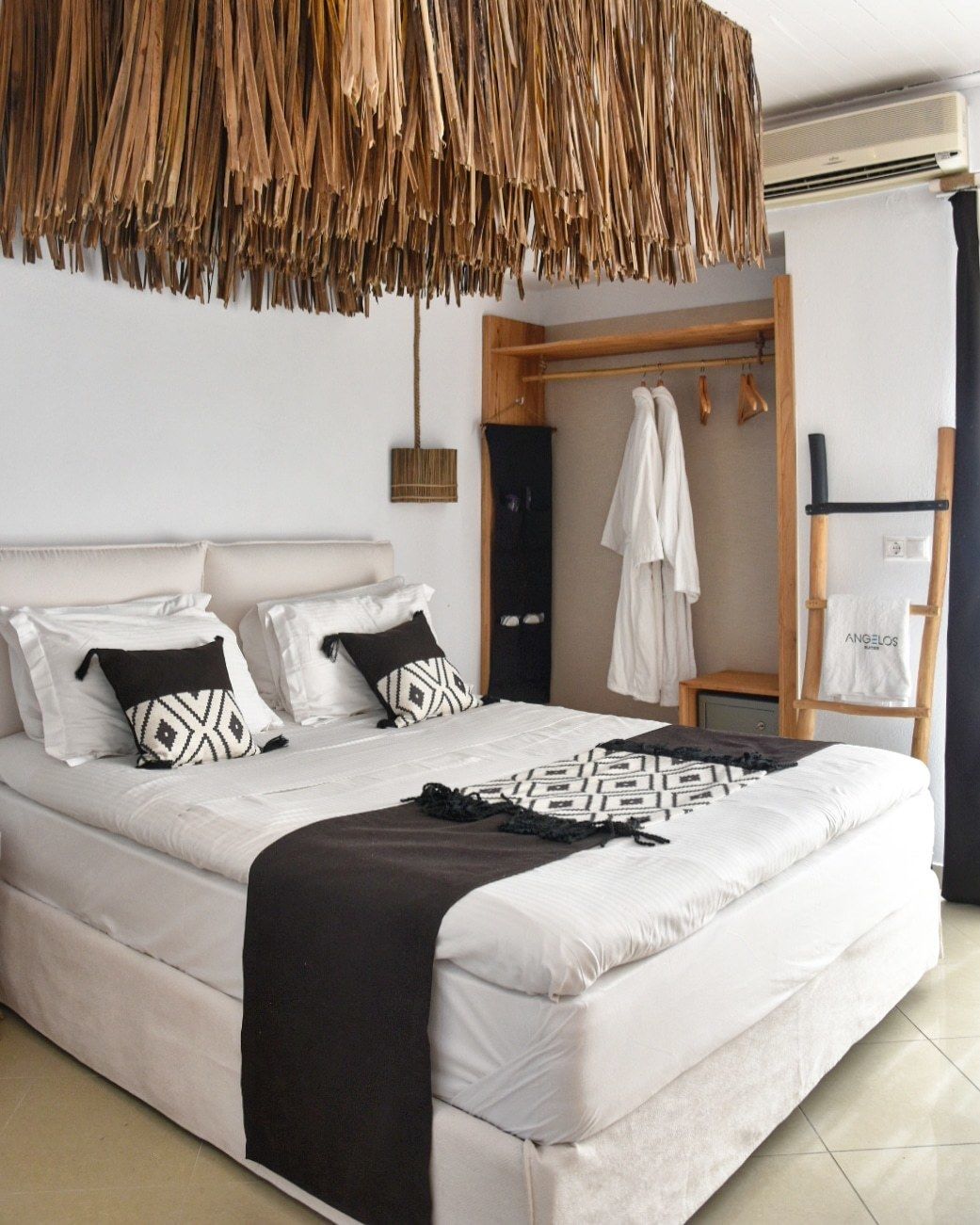 A bedroom with a large bed, a hanging rattan headboard, a wooden wardrobe, and a white towel hanging on a wooden rack.