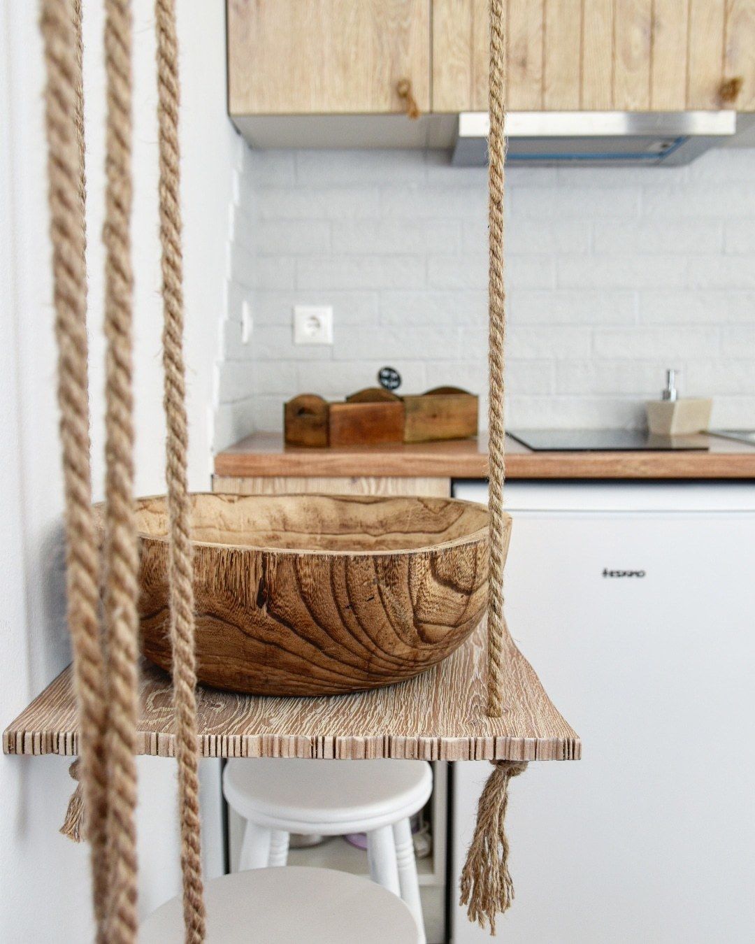 A kitchen with a hanging wooden bowl suspended by ropes, a white countertop, and a white cabinet in the background.