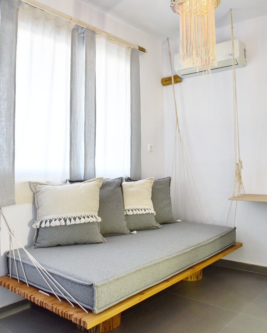 Una habitación moderna con una cama suspendida, una lámpara colgante y un ventanal con cortinas traslúcidas.
