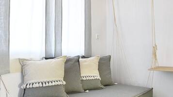 Una habitación moderna con una cama suspendida, una lámpara colgante y un ventanal con cortinas traslúcidas.