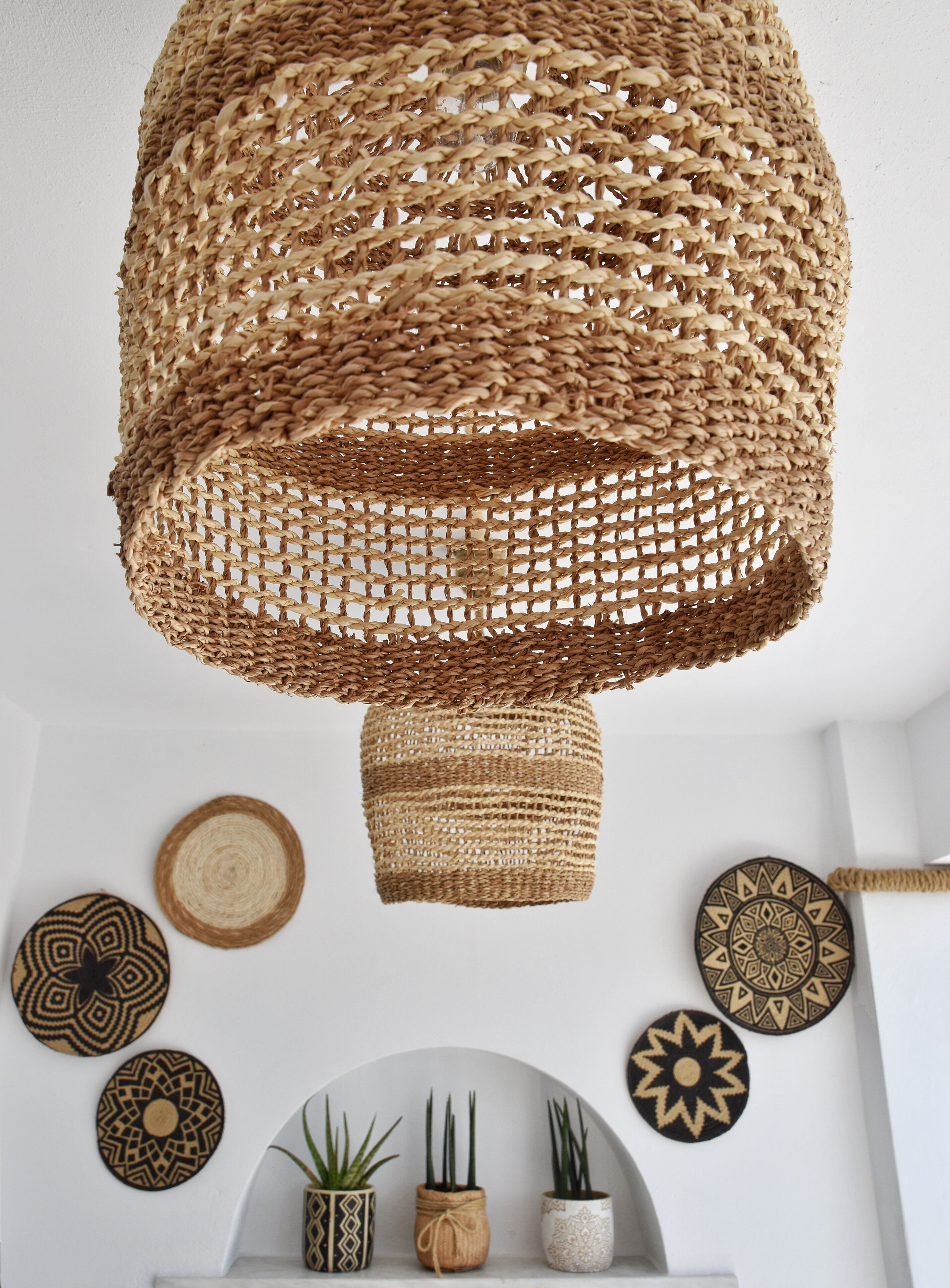 A woven basket hanging from the ceiling, surrounded by various woven wall hangings and potted plants.
